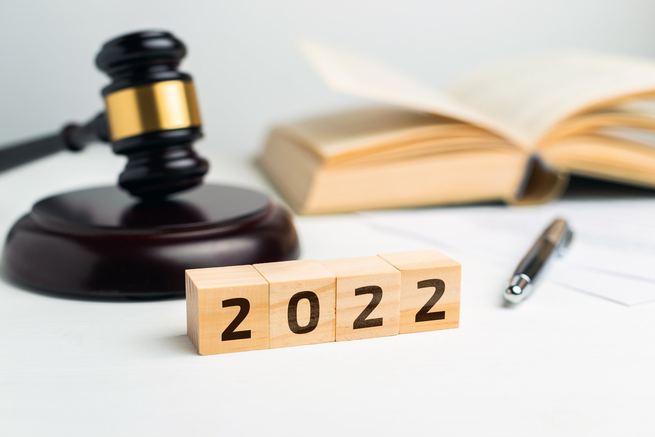 A table with a gavel, pen, open book, and blocks with the year 2022 symbolized. 