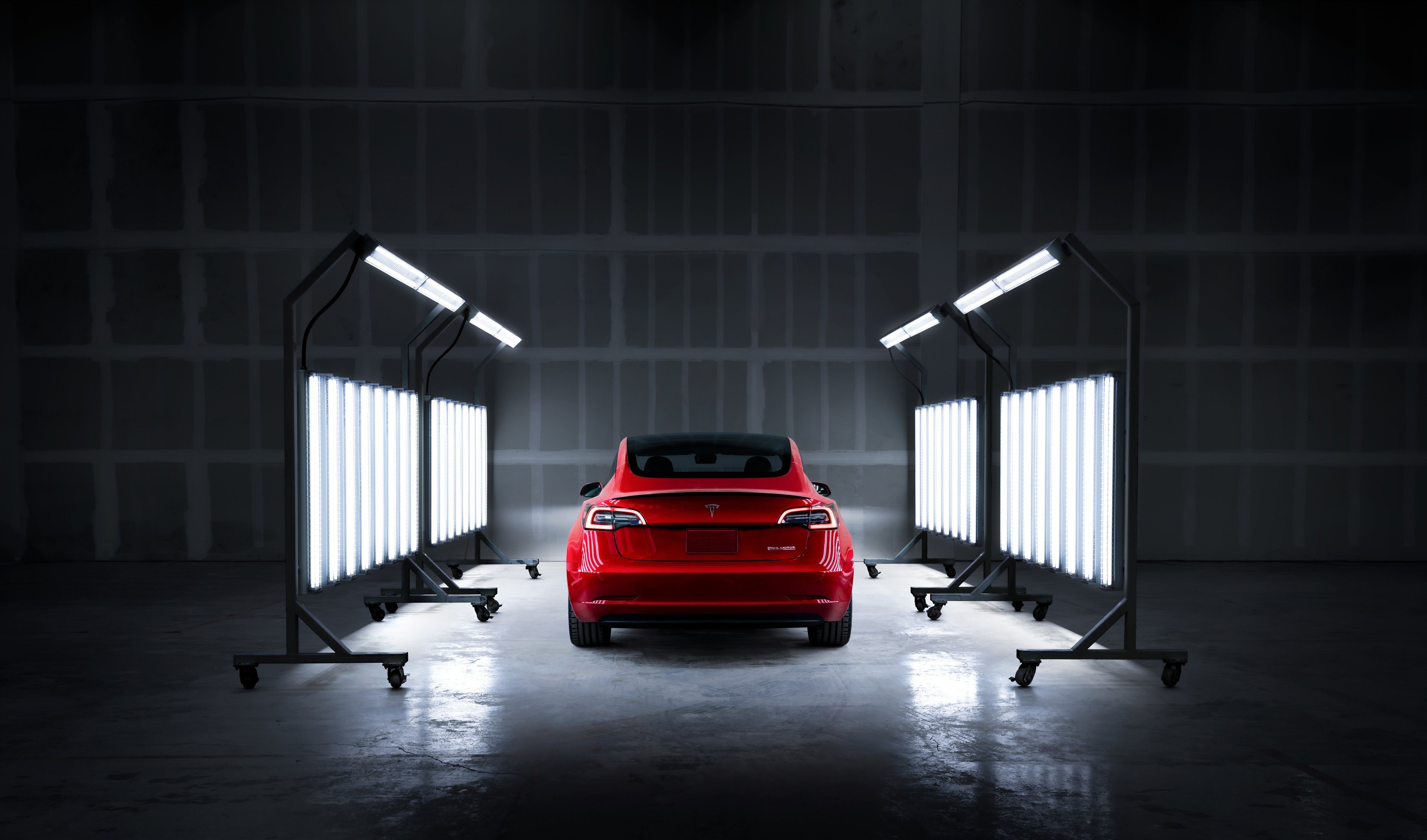 Rear view of red Tesla under body shop service lights.  