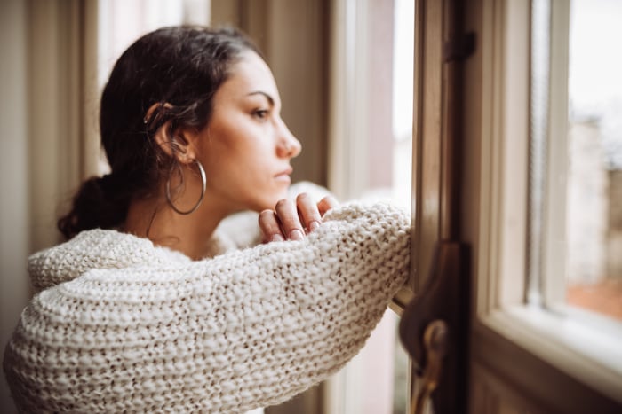 Person with a serious expression looking out a window.