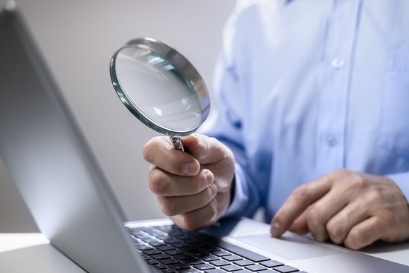 Man holds magnifying glass up to laptop. 