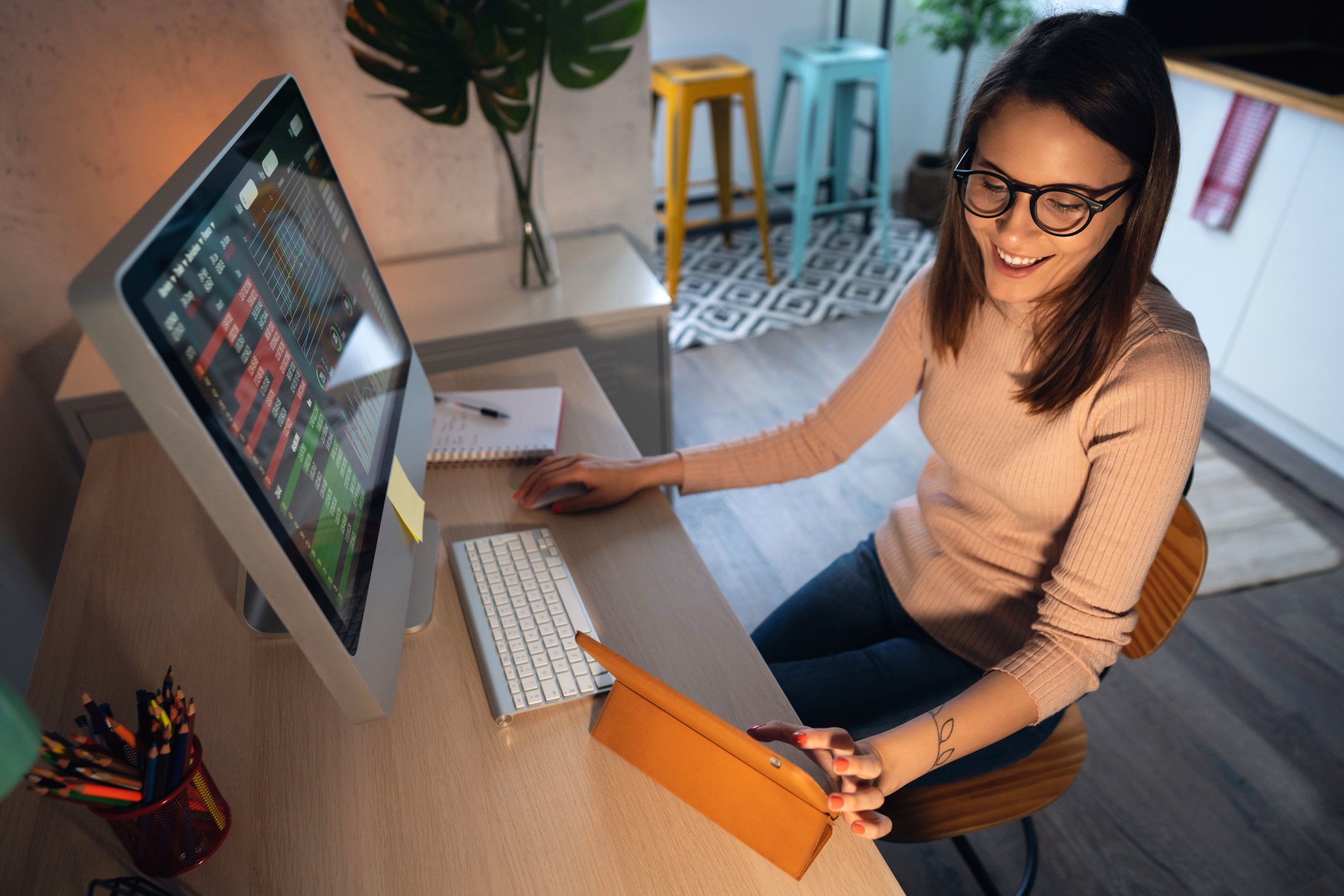 Woman at a desk working on a computer and scrolling on a tablet.