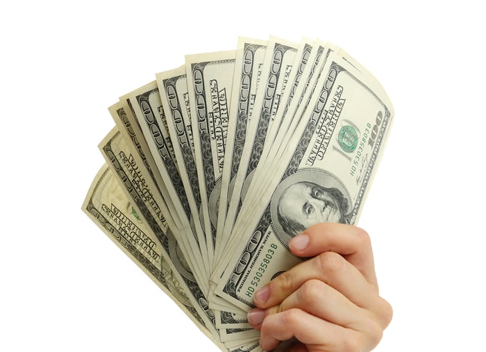 A person holds hundred-dollar U.S. banknotes in their hand.