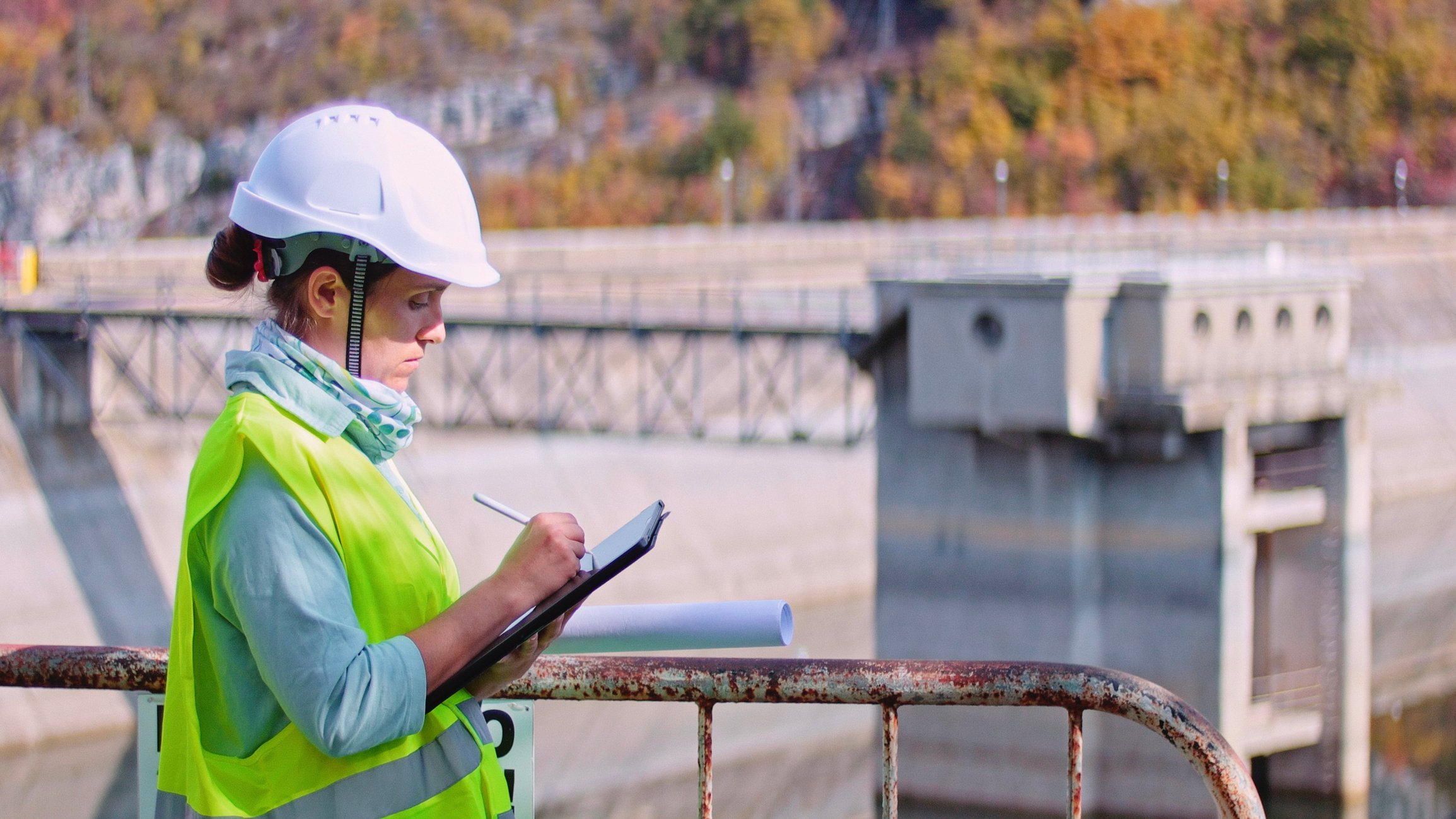 A woman in a hard hat writes notes at a hydroelectric power plant.
