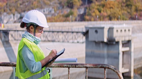 A woman in a hard hat writes notes at a hydroelectric power plant.