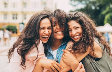 Three young women laughing and hugging