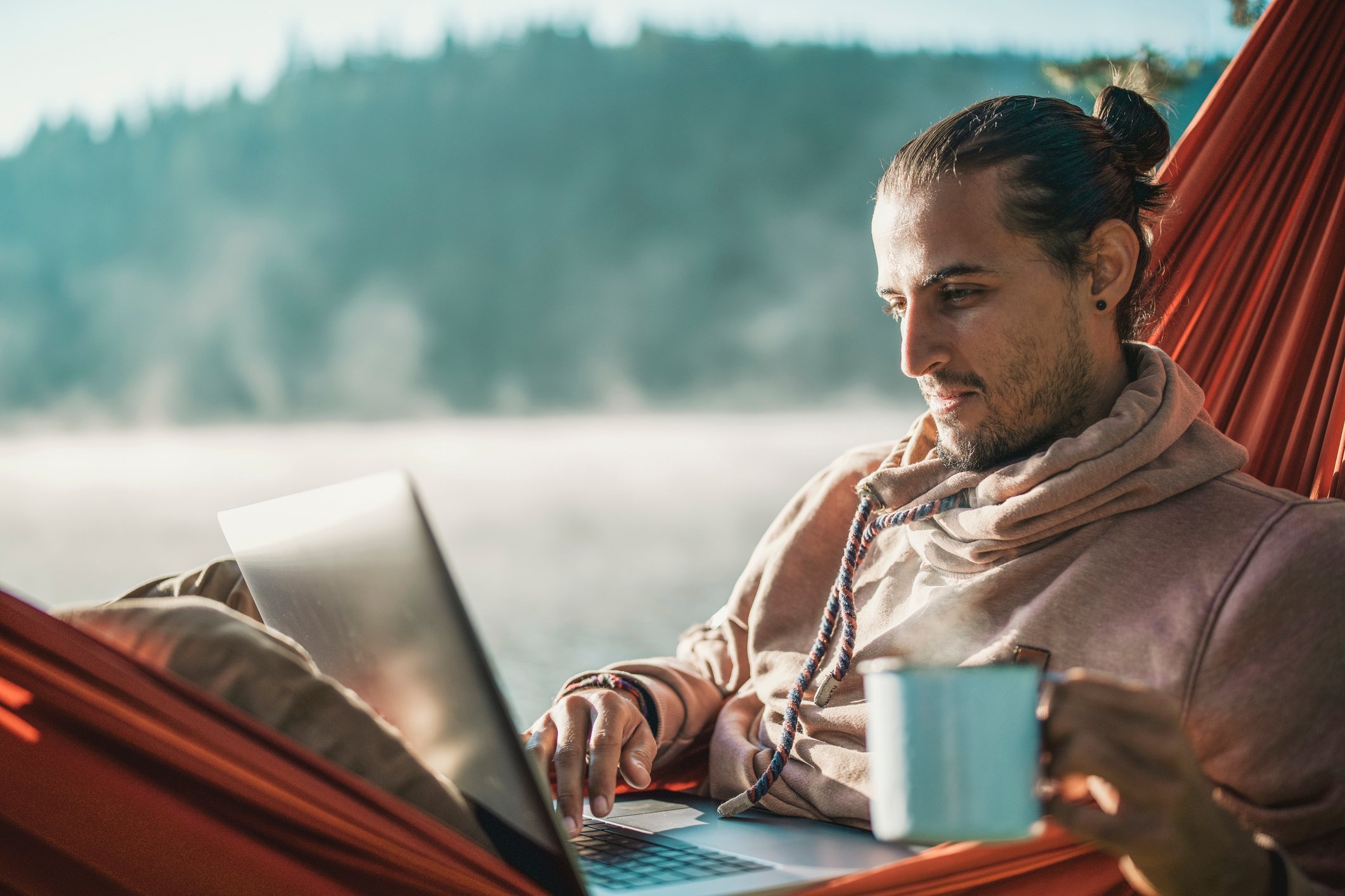 Investor checks stock portfolio on laptop while sitting in hammock overlooking lake