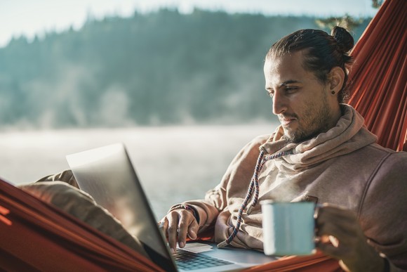 Investor checks stock portfolio on laptop while sitting in hammock overlooking lake
