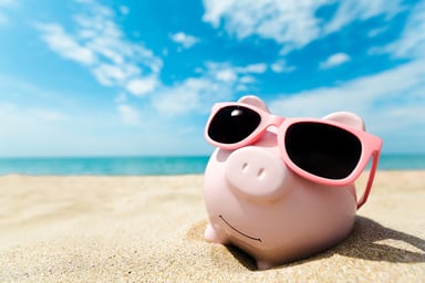 A piggybank on the beach wearing sunglasses.