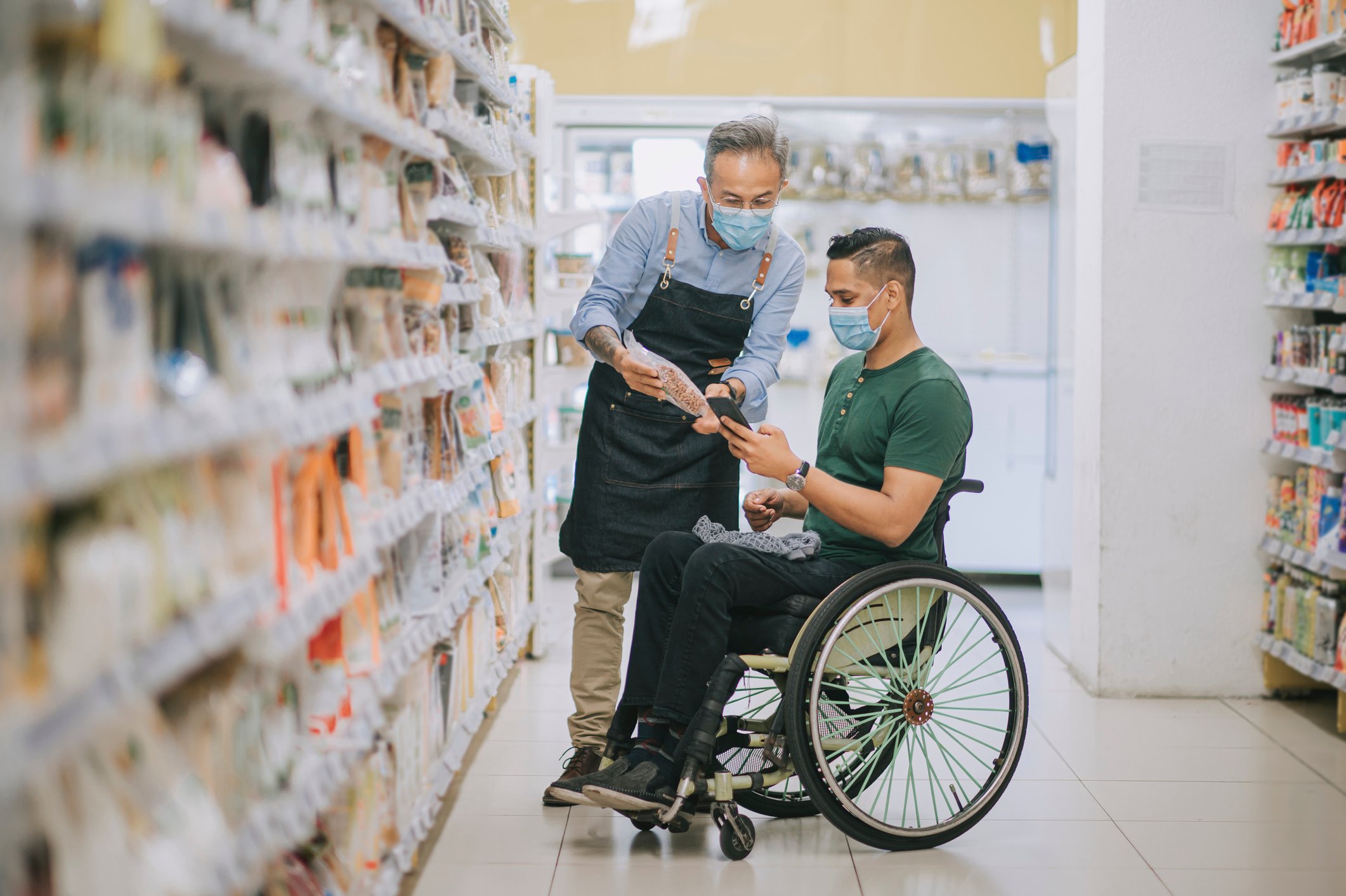 A grocery store worker helps a customer find food in an aisle.
