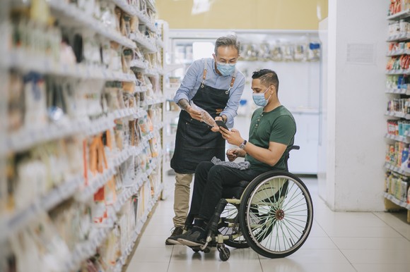 A grocery store worker helps a customer find food in an aisle.