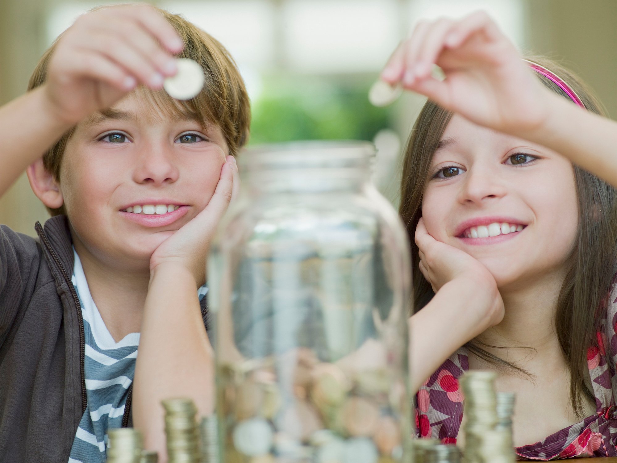 Two young kids put coins in a jar. 