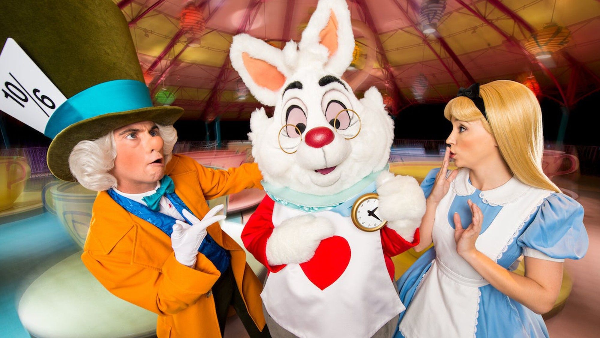 Alice in Wonderland, Mad Hatter, and Rabbit in front of the spinning tea cups ride at Disney World.