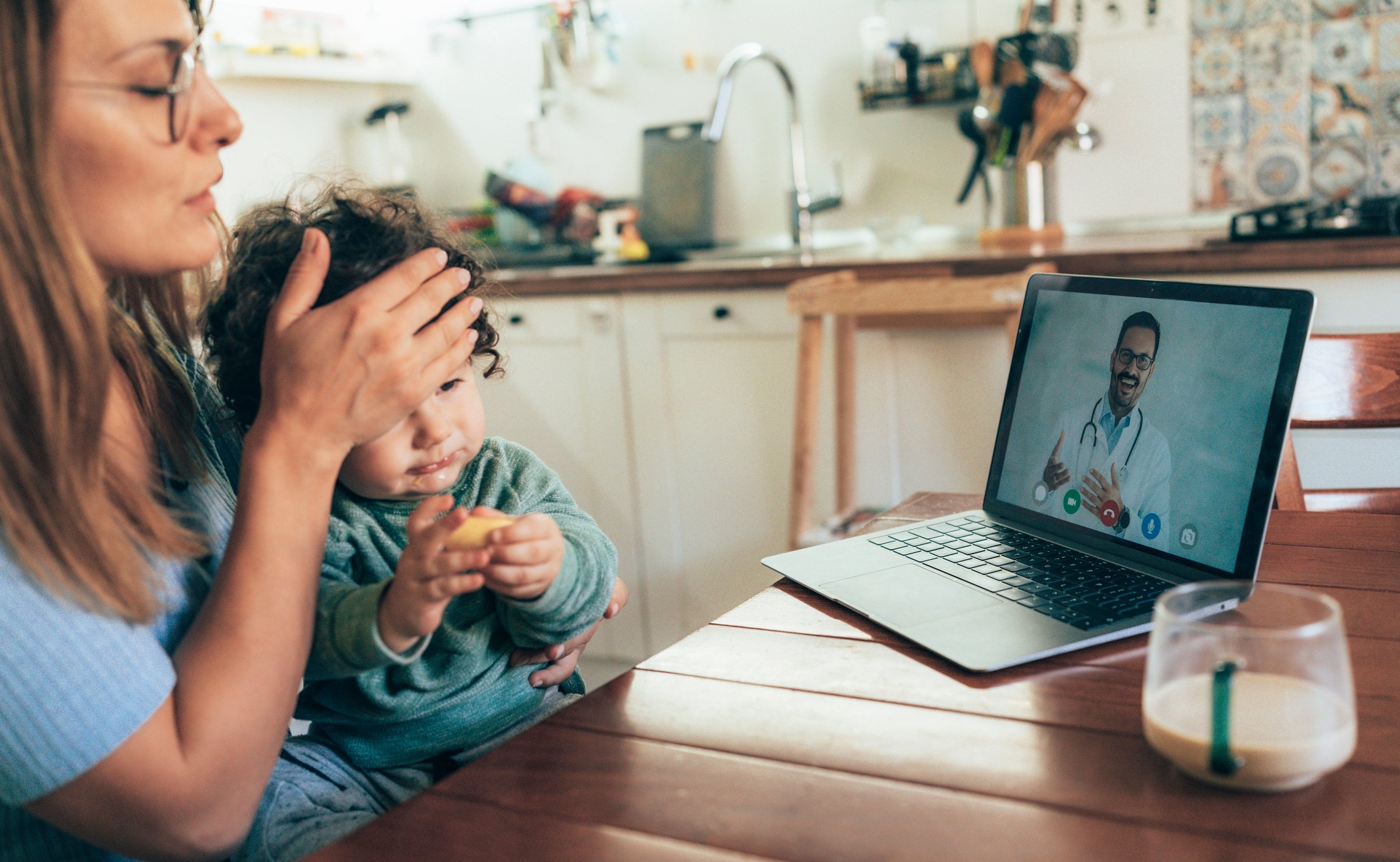 Person and sick baby talking to doctor via laptop.