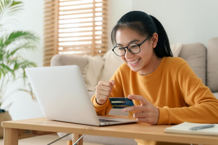 Person holding a credit card while smiling at an laptop screen.