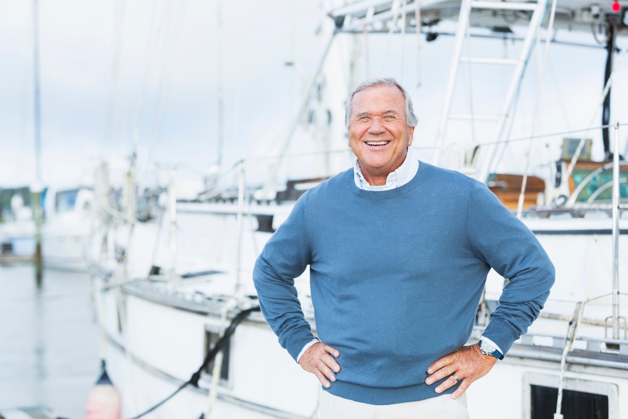 Affluent smiling man in a sweater standing on a dock in front of his yacht.