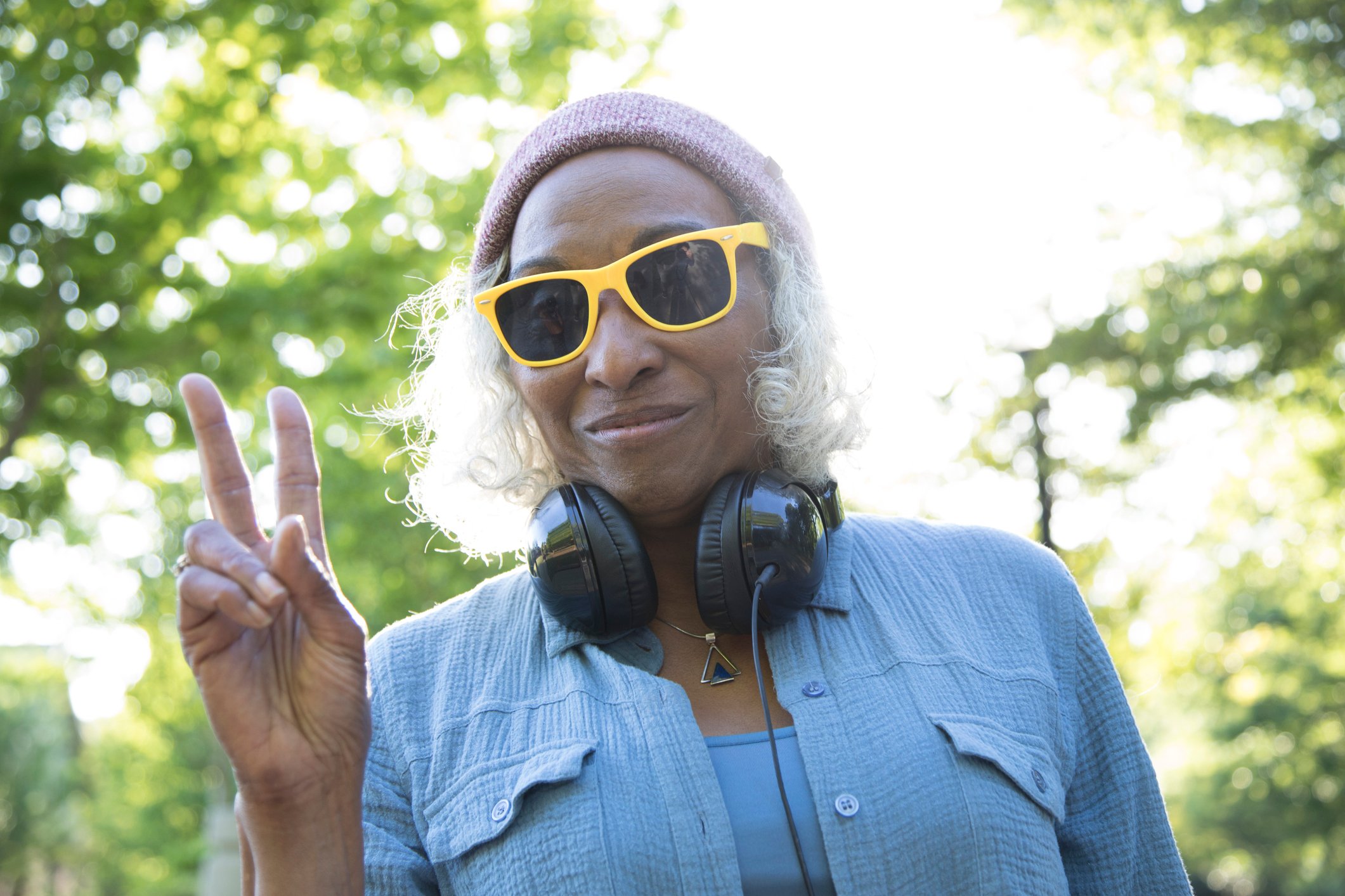 An older, possibly retired person wearing yellow sunglasses makes a peace sign.