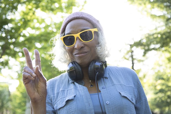 An older, possibly retired person wearing yellow sunglasses makes a peace sign.