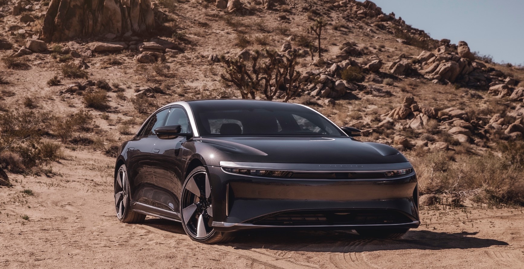 Lucid Air parked in a desert scrub environment with a hill rising behind it.