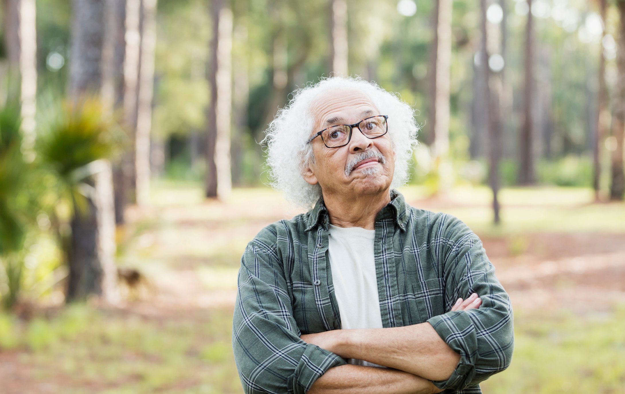 Elderly person with crossed arms standing in a forest. 