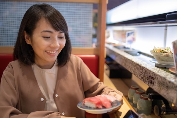 A customer takes a plate of sushi from a conveyor belt.
