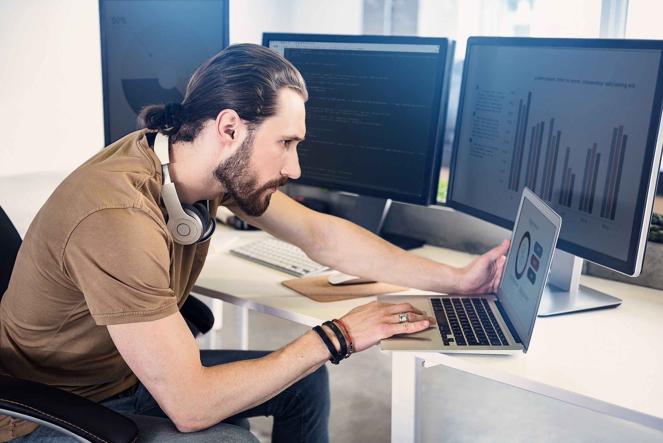 A person working on a laptop in front of two computer monitors.