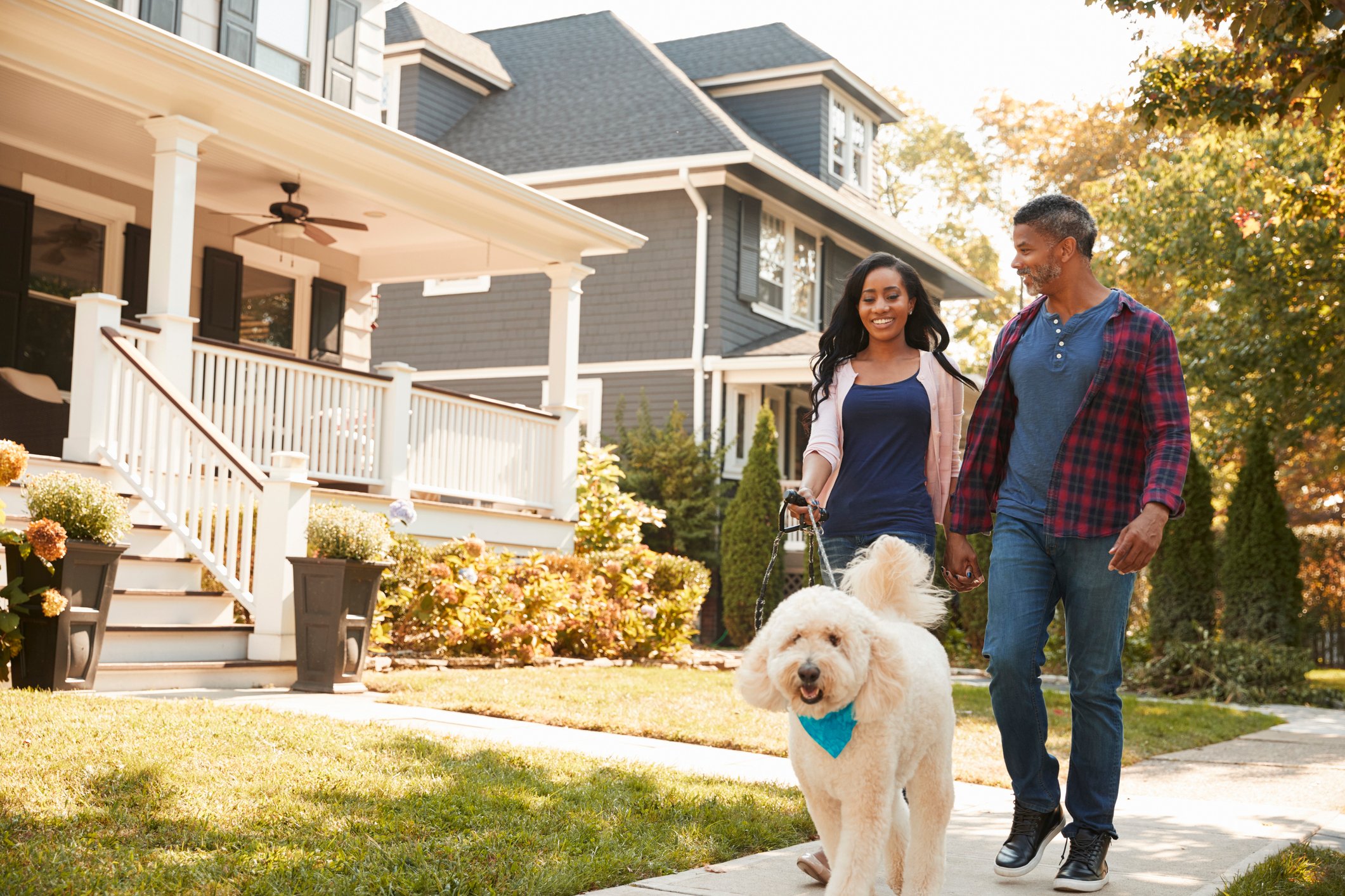 Two people and a dog walking past a house. 