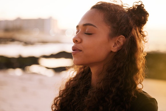 Person with eyes closed breathing deeply while standing on the beach.