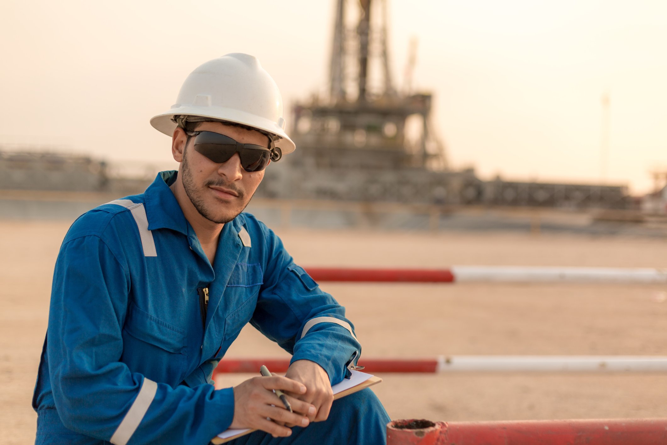 An oil engineer takes notes at a job site near an oil rig. 