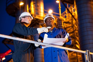 Two people look at plans at a refinery at night.