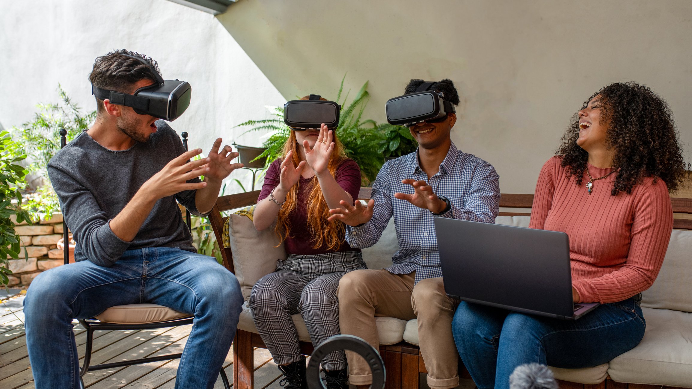 Three people use virtual reality headsets while another individual looks on and laughs.
