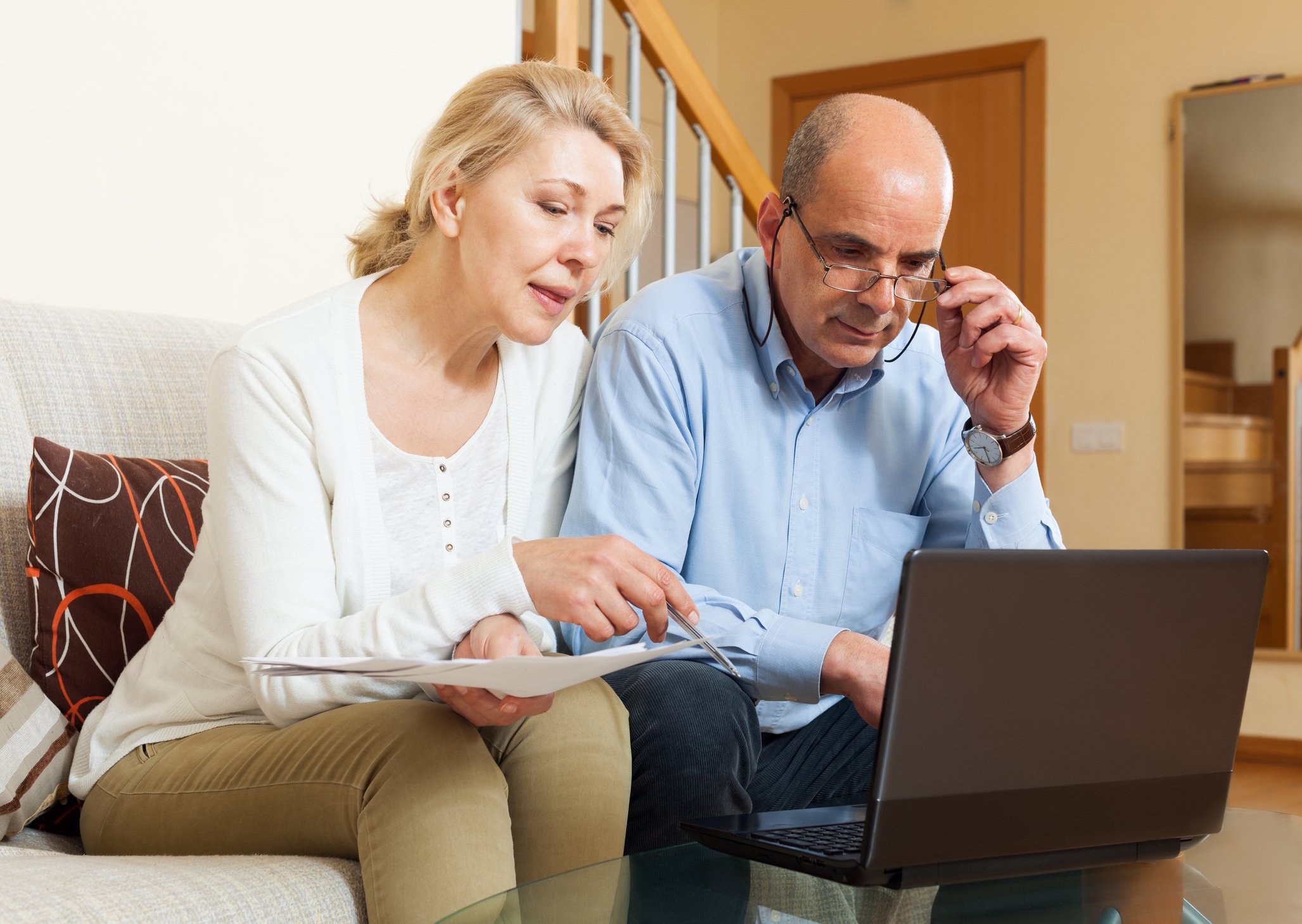 Couple reviews paperwork and information on laptop screen at home.