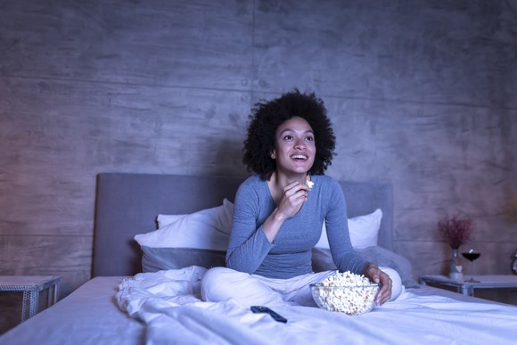 A young person eating popcorn in bed while watching something on TV.