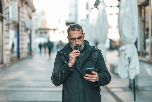 Smoker walking down the street using an IQOS device.
