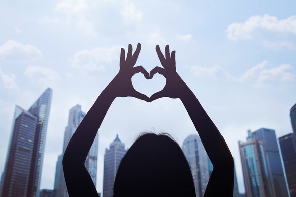 Person holding hands into heart above city sky line.