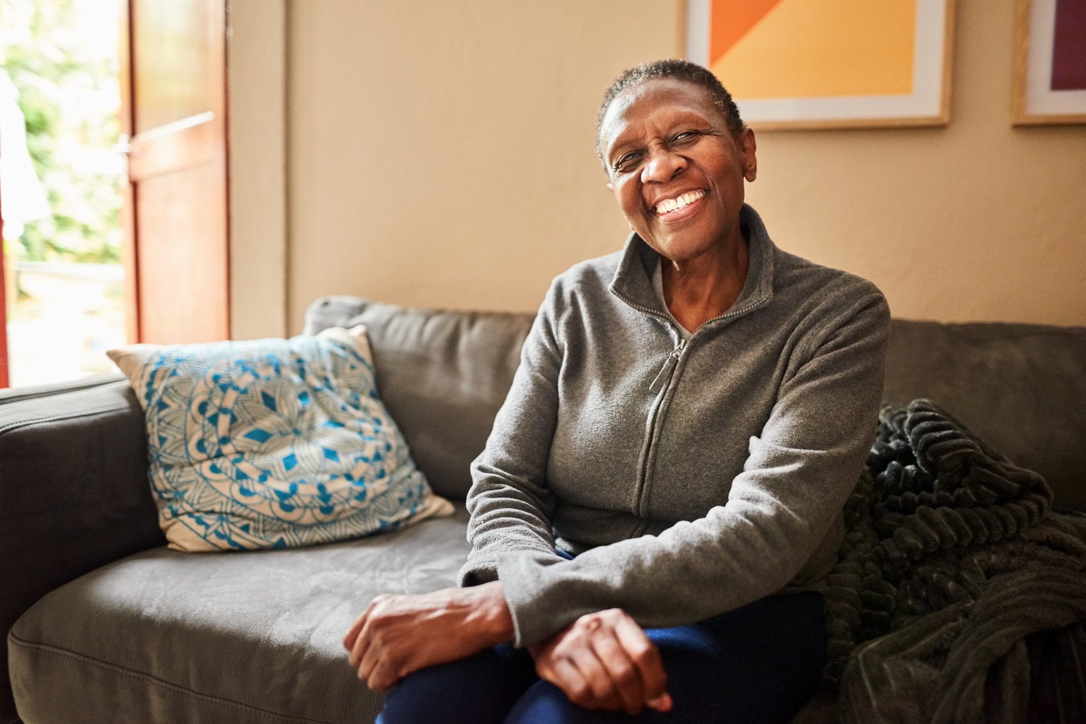 A person is seated on a sofa, smiling broadly.