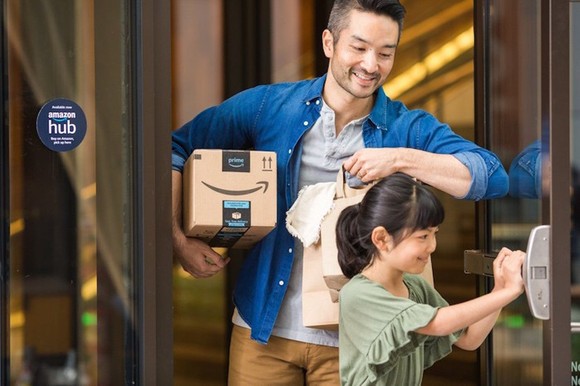 A parent carrying an Amazon package under their right arm while child holds open a door.