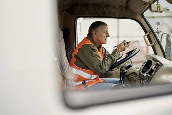 Person wearing a safety vest and sitting in truck while talking on a cell phone.
