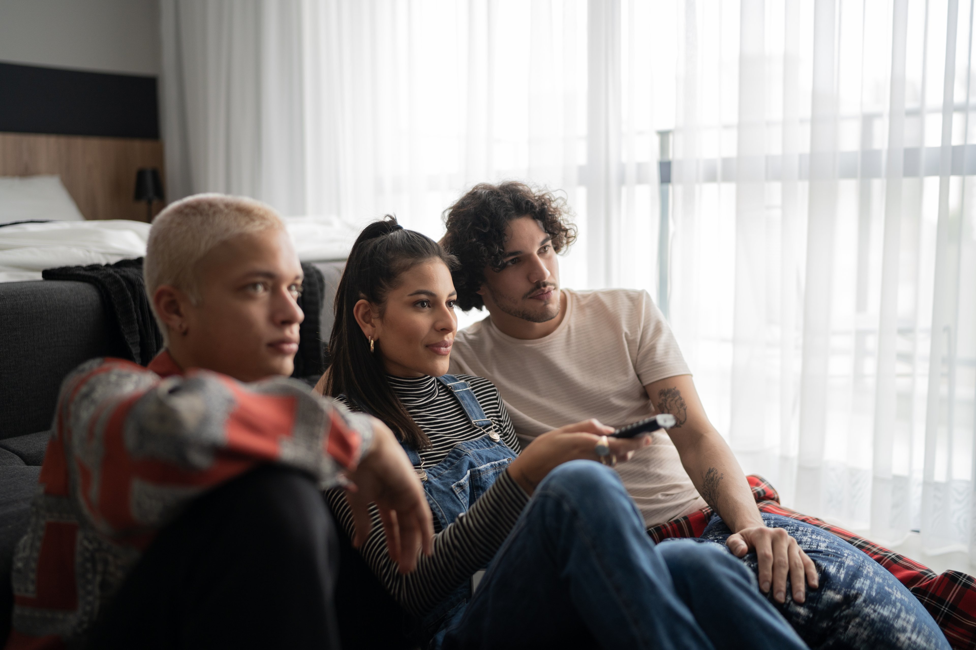 Three young people sitting on a couch, watching TV.
