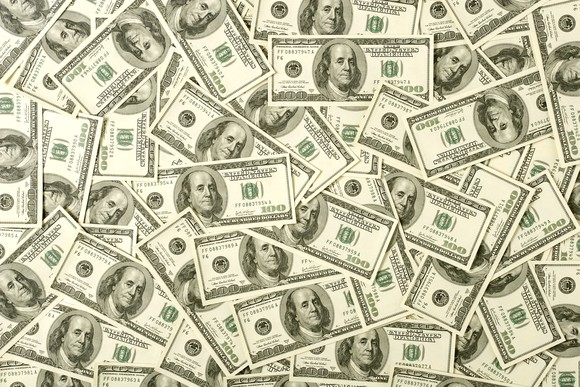 Dozens of $100 bills scattered all over a flat surface.