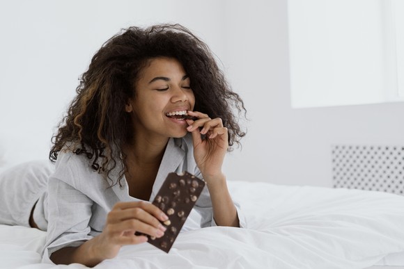 Person smiling while eating a candy bar in bed.