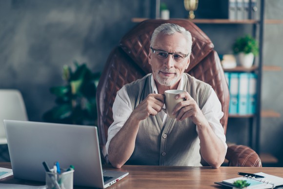 A person sitting in a chair drinking coffee in front of a laptop.