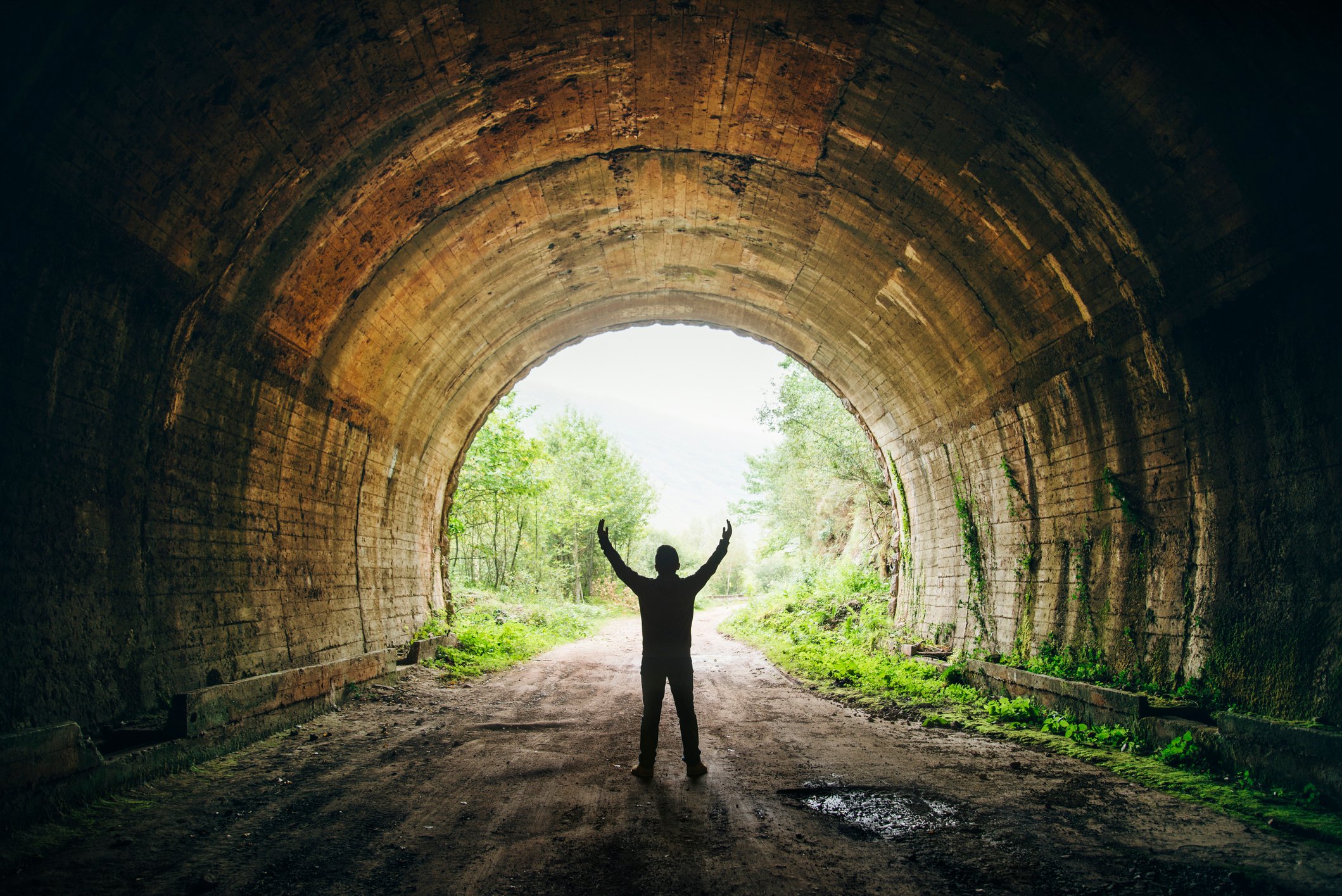 Silhouetted person cheering while looking at the light at the end of a tunnel.