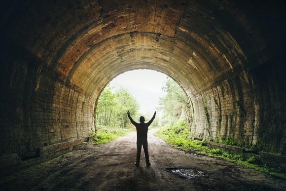 Silhouetted person cheering while looking at the light at the end of a tunnel.