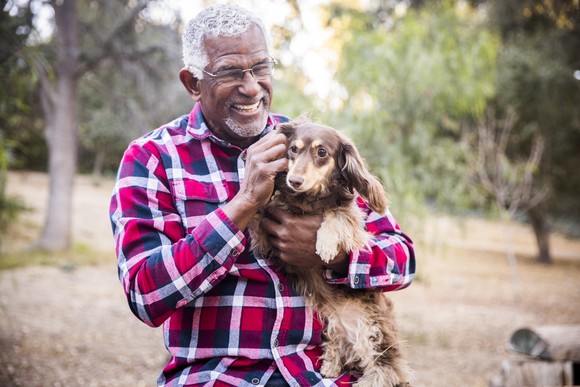 A person smiles while holding a dog outdoors.