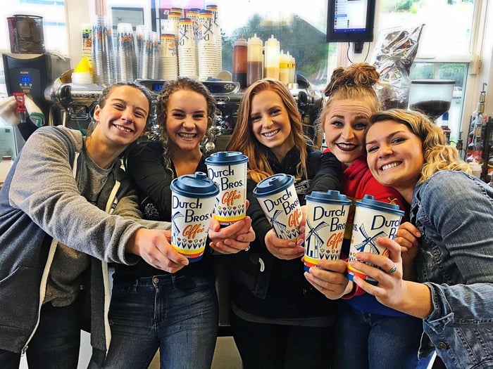 Five people smile and hold up Dutch Bros coffee cups.