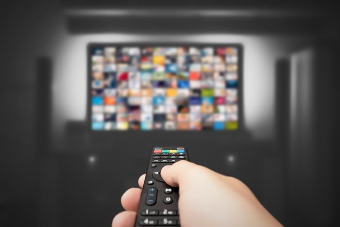 A hand holding a remote in front of a TV.