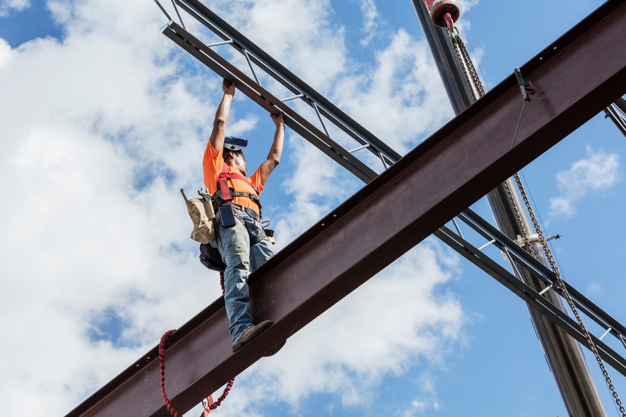 A person wearing a hard hat works on a steel girder. 