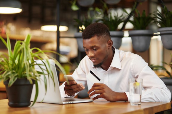 A person sits at a desk holding a smartphone in one hand and a credit card in the other.