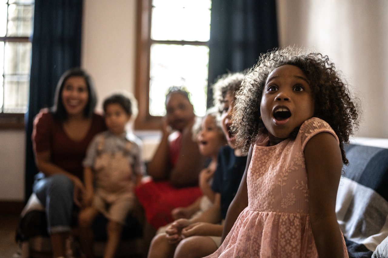Adults and children, all sitting together, watching TV.