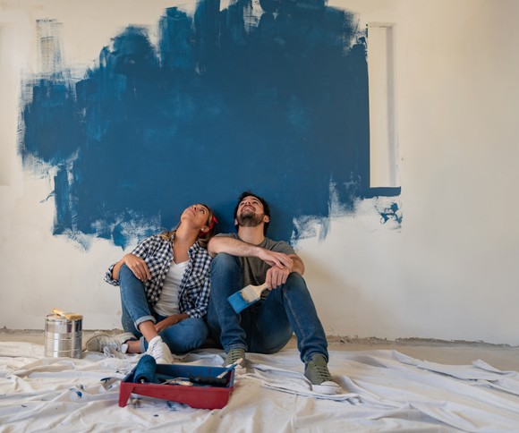 Two people resting from painting wall in empty home.